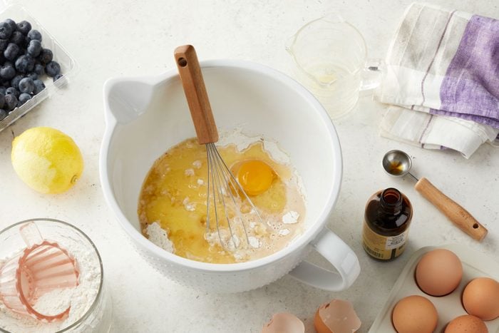 milk, butter, eggs and a spatula inside a large bowl place on a kitchen countertop.