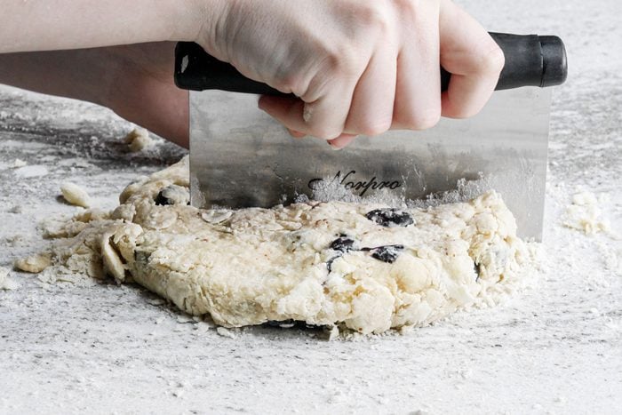 a person cutting Blueberry Scones Dough into pieces using a bench scraper on marble surface