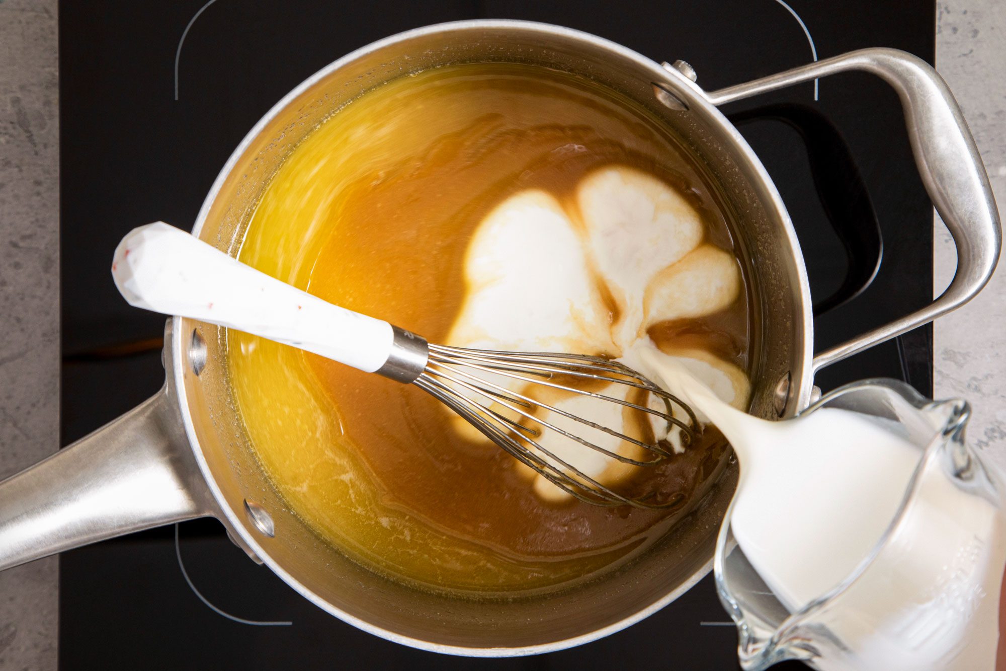 pouring cream into melted butter and brown sugar in a saucepan on induction cooktop