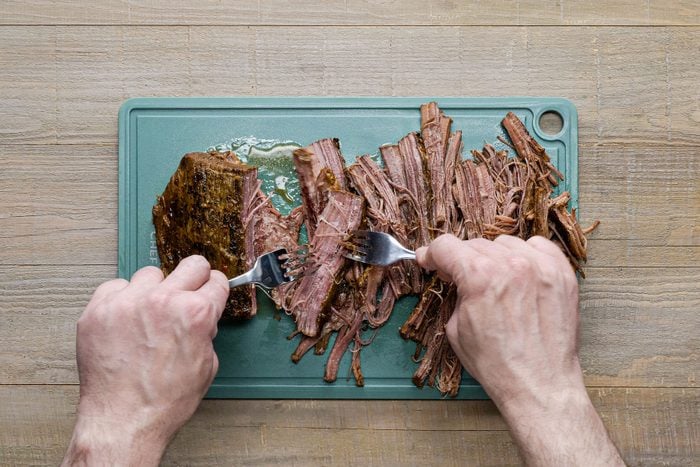 Shredding the brisket with forks on chopping board