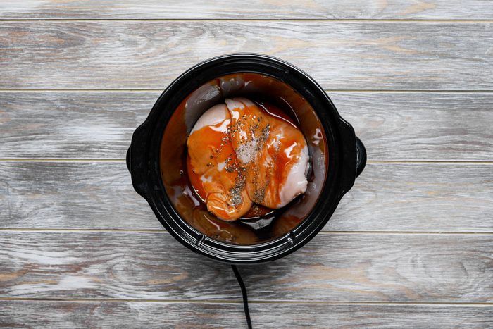 Chicken breasts with hot sauce and pepper mixed in a slow cooker.