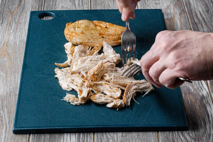 Shreding chicken with two forks on a tray placed on a wooden table
