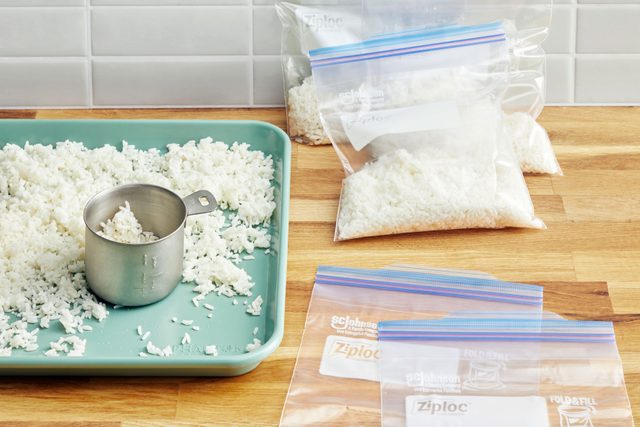 cooked white rice being transferred from a baking sheet into plastic freezer bags on a kitchen counter