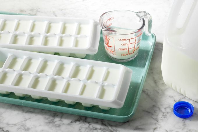 ice cube trays filled with milk are on a baking sheet near a gallon container of milk on a marble countertop