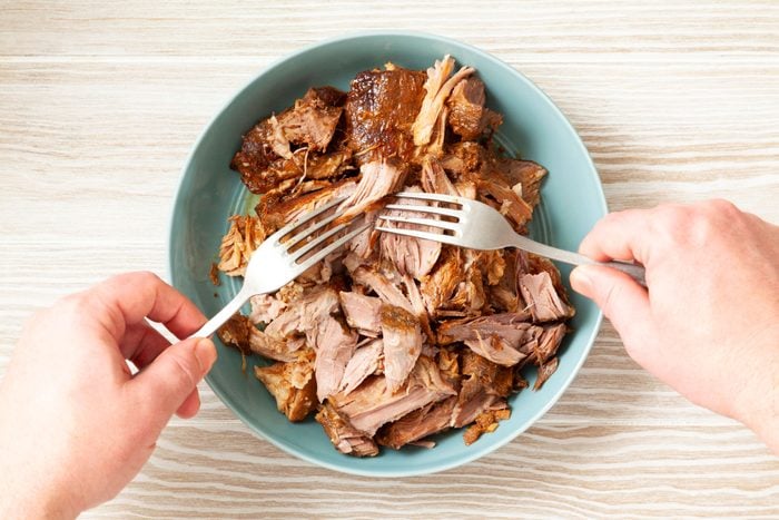 Shreding the roasted pork with a fork in a small bowl