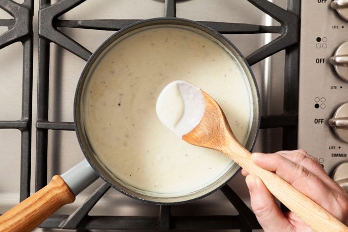 Stirring the milk mixture in a large saucepan using a wooden spatula