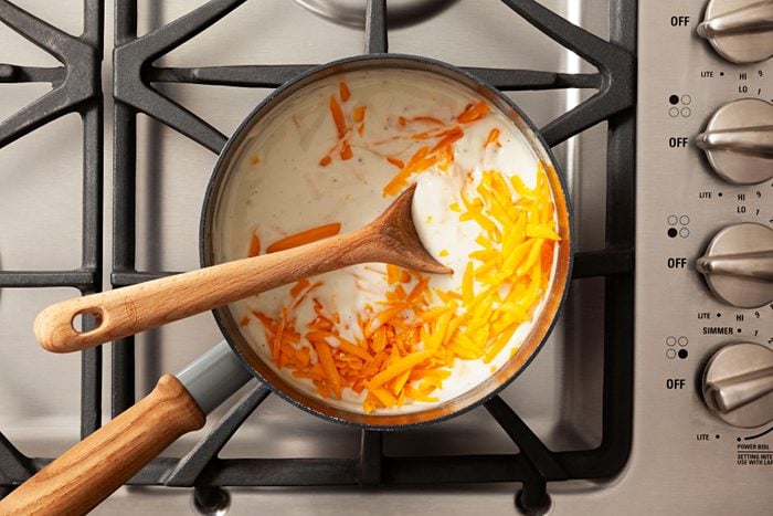 Stirring cheese in the milk mixture in a large sauce pan