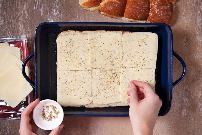 Sprinkling oregano on cheese slice on a baking tray
