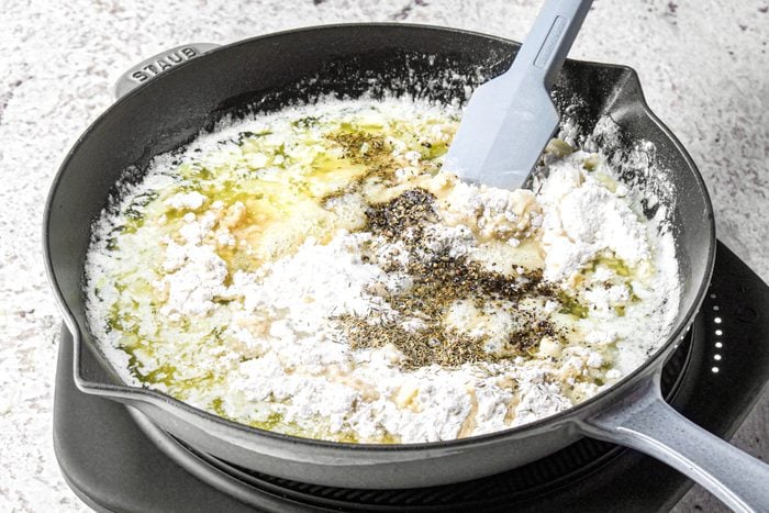 Stirring flour butter and other ingredients with a spatula in a large skillet.