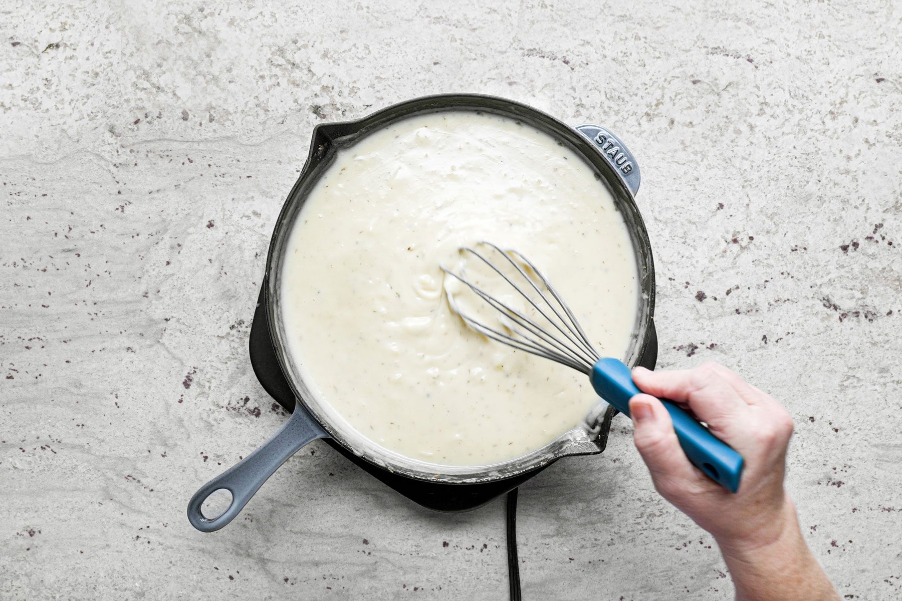 Stirring the mixture with spatula in a large skillet on a marble countertop.