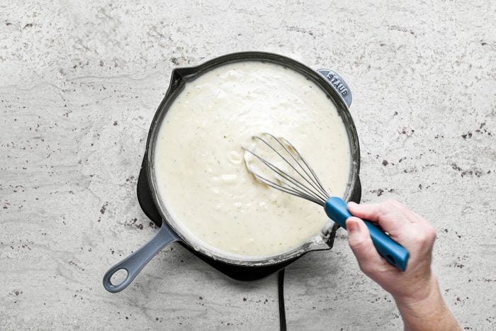 Stirring the mixture with spatula in a large skillet on a marble countertop.