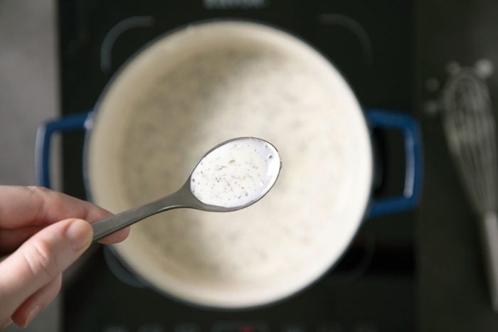 A person holding a spoon filled with white gravy