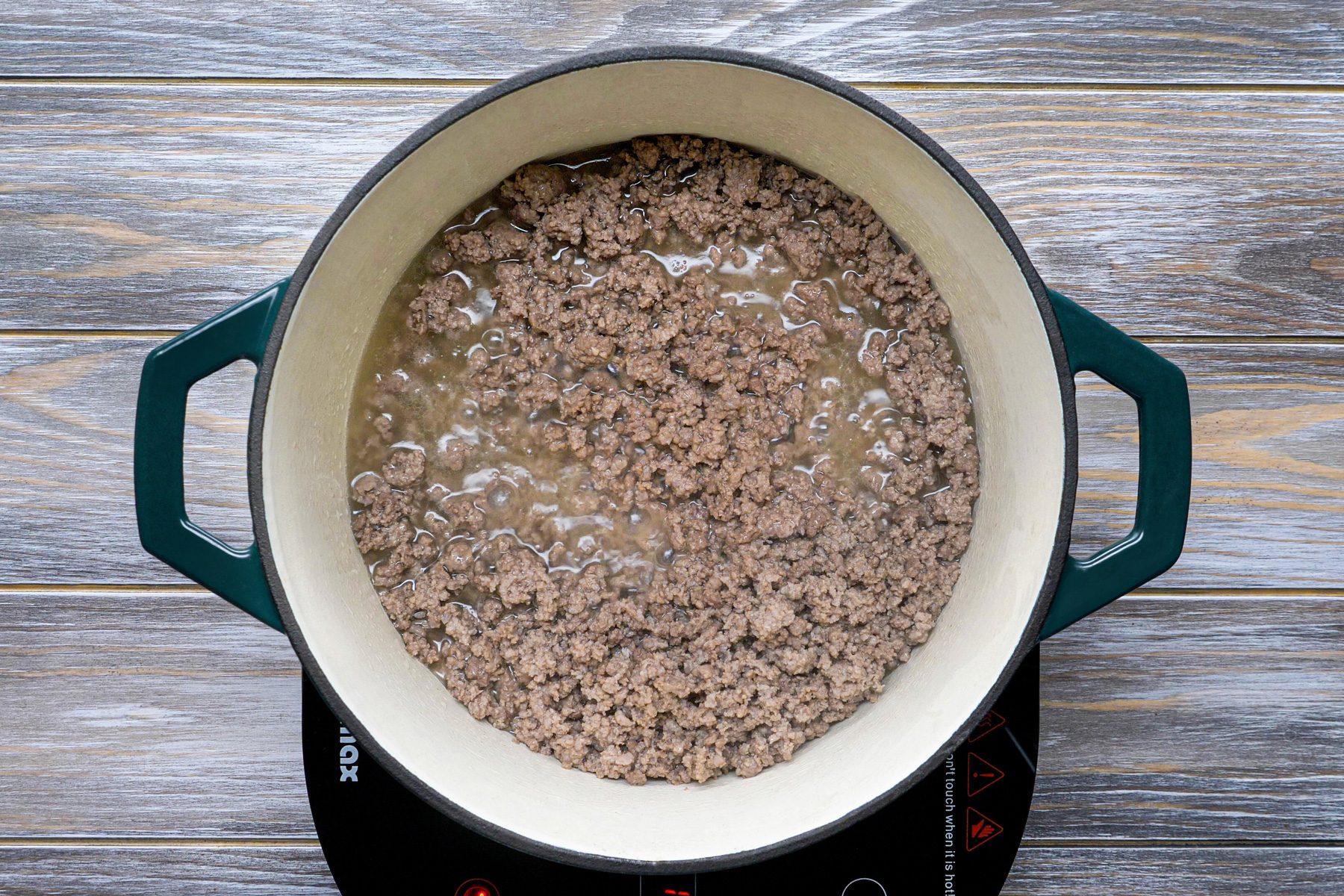 A Dutch oven with beef crumbles cooking on an induction stove