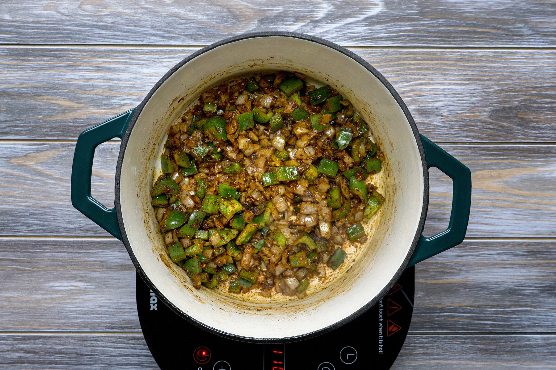 Stirring green peppers, onions, and other ingredients in a Dutch oven