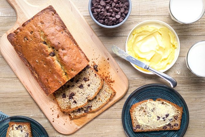 Chocolate chip banana bread on a wooden chopping board and chocolate chip banana bread on a small plate and a bowl of butter next to it