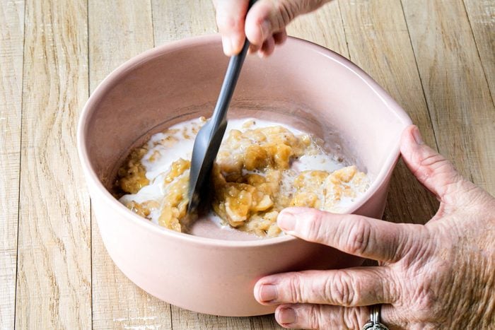 mixing banana and milk together in a large bowl on wooden surface