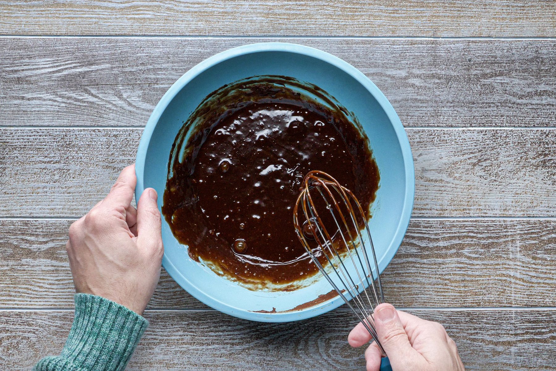 A person whisking a chocolate liquid in a blue bowl