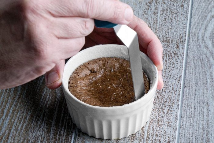 A person holding a knife over a white ramekin