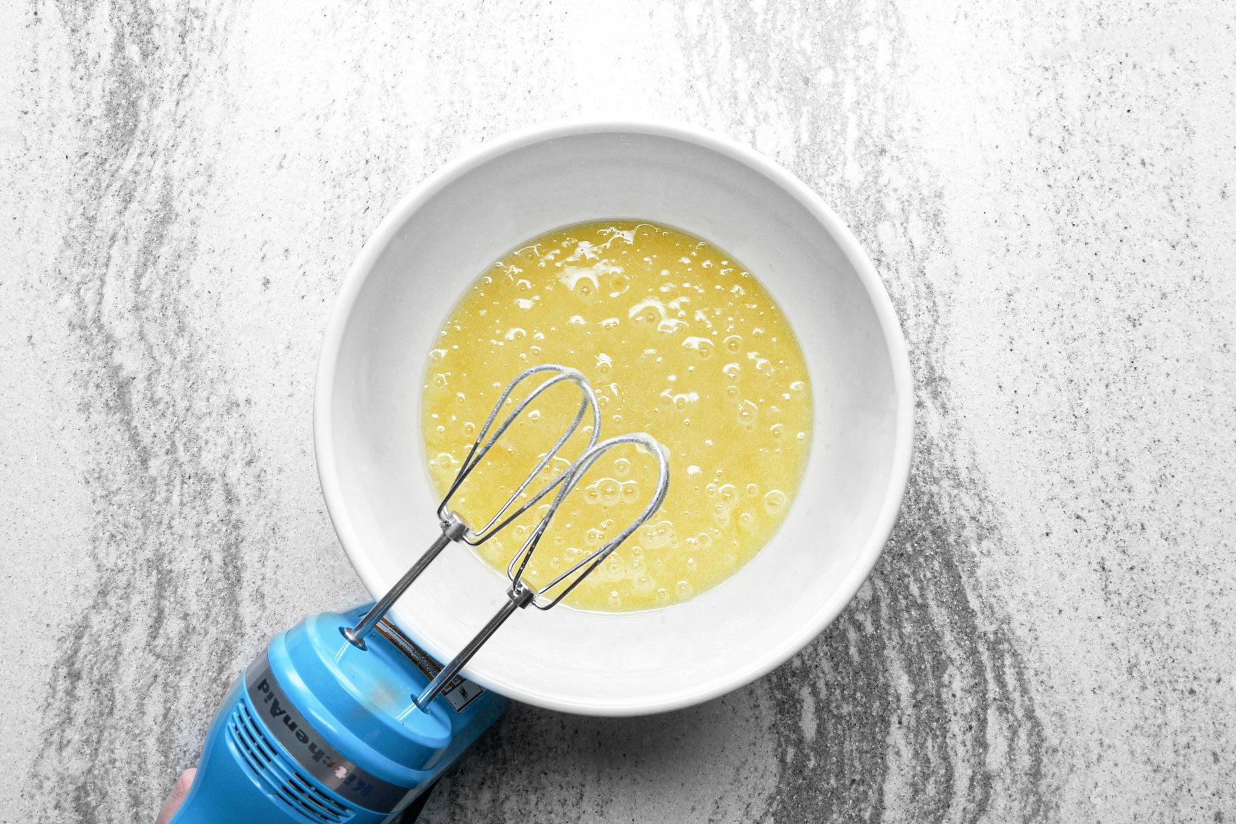sugar, oil, eggs and vanilla mixed in a bowl with a hand blender