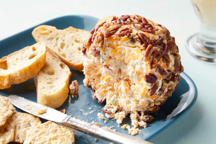 A Christmas cheese ball with pecans and cheese slices on a plate
