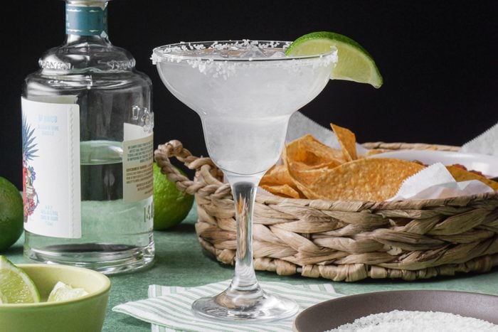 A glass of classic margarita with lime wedges and chips