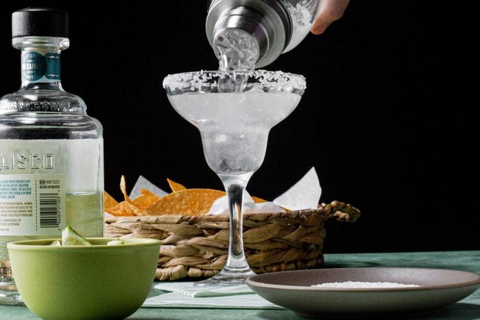 A hand pouring prepared tequila into a margarita glass