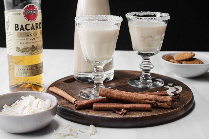 Coquito drink in glass on a wooden tray and a bottle of run on side