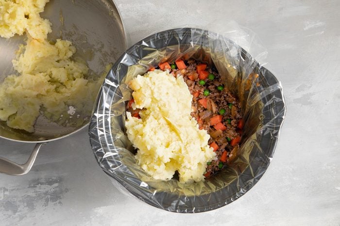 Spreading mashed potatoes over meat mixture in slow cooker
