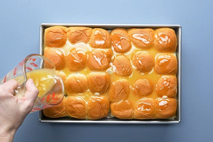 Drizzling the butter over the rolls in a baking dish