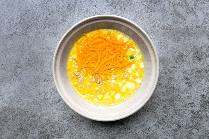 Eggs and cheese mixed in a large bowl, placed on a marble surface. 