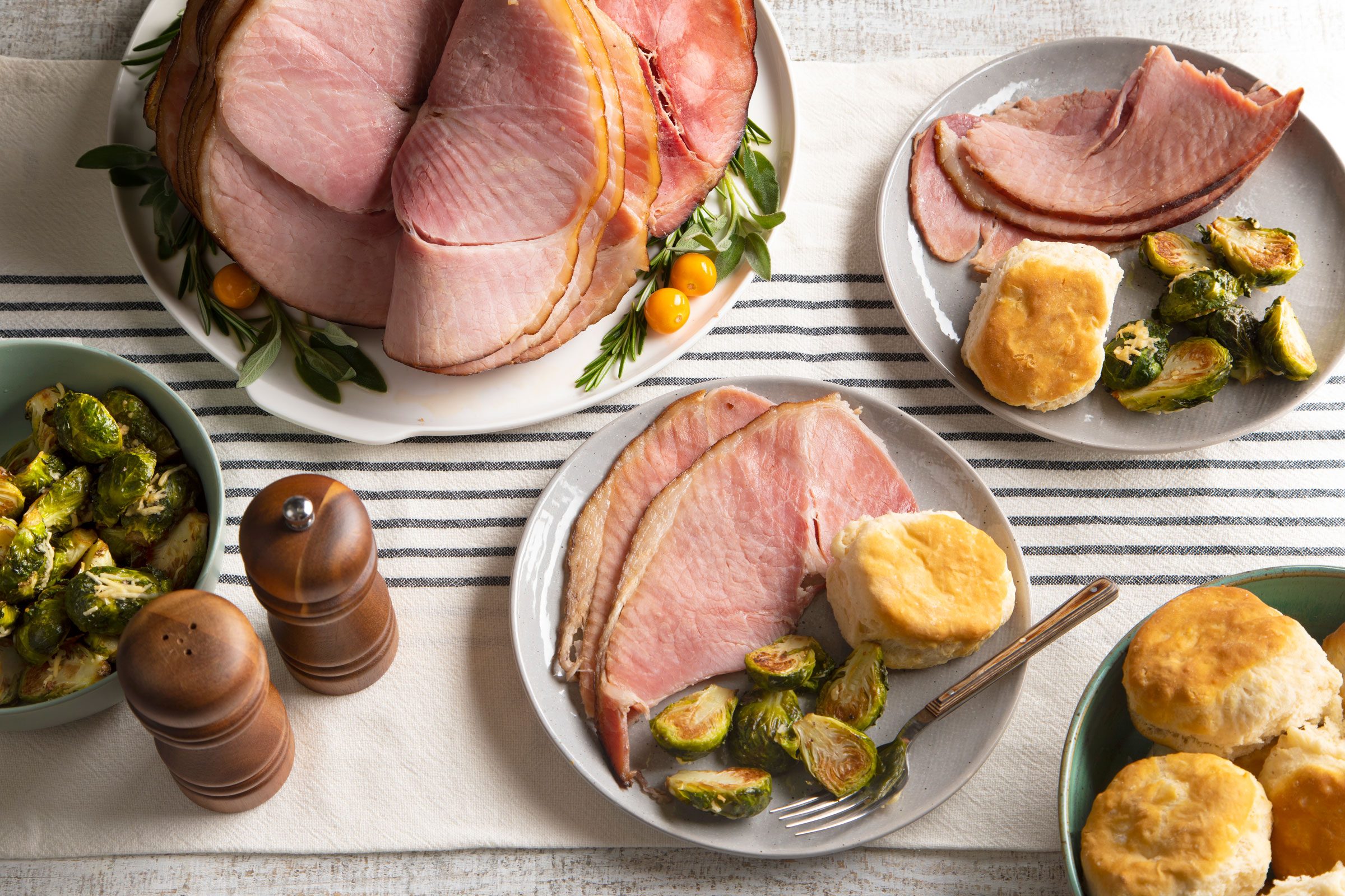 Baked Spiral Ham served on two small plates with a side of brussel sprouts and rolls