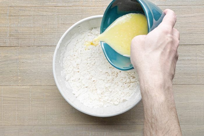 A person adding whisked eggs in bowl of flour