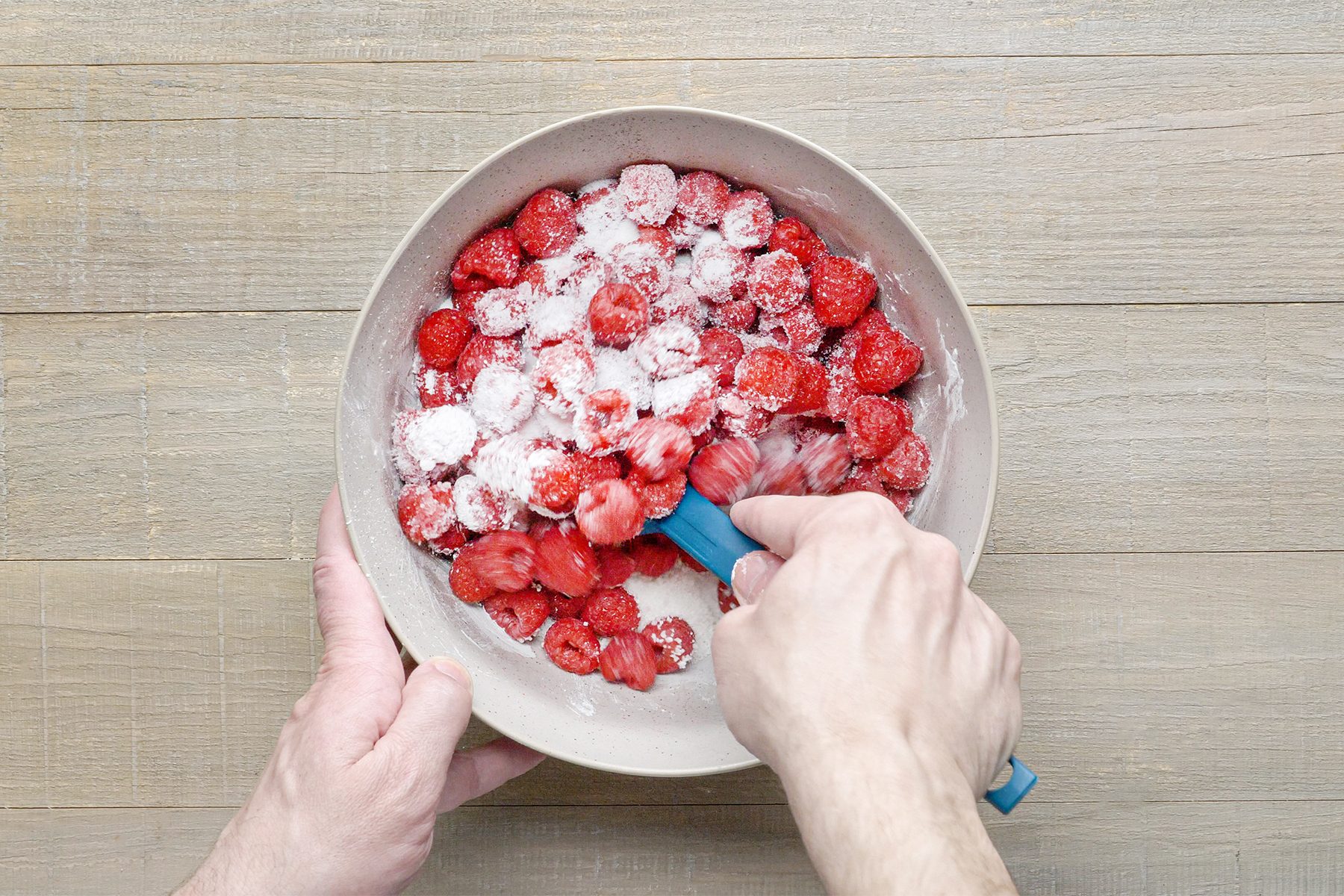a person mixing sugar, tapioca, cornstarch and raspberries in bowl