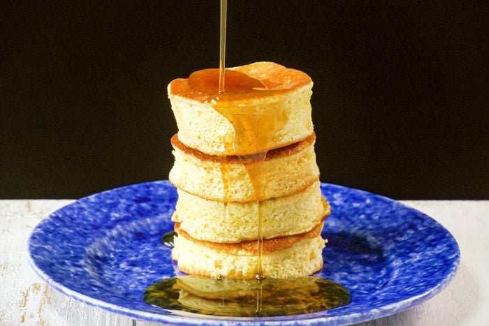 Pouring Honey Over Japanese Pancakes Placed On A Fancy Blue Plate On White Painted Wooden Surface