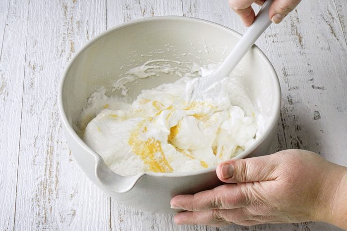 Mixing Beaten Eggs with Flour Mixture In A Large White Bowl on White Painted Wooden Surface