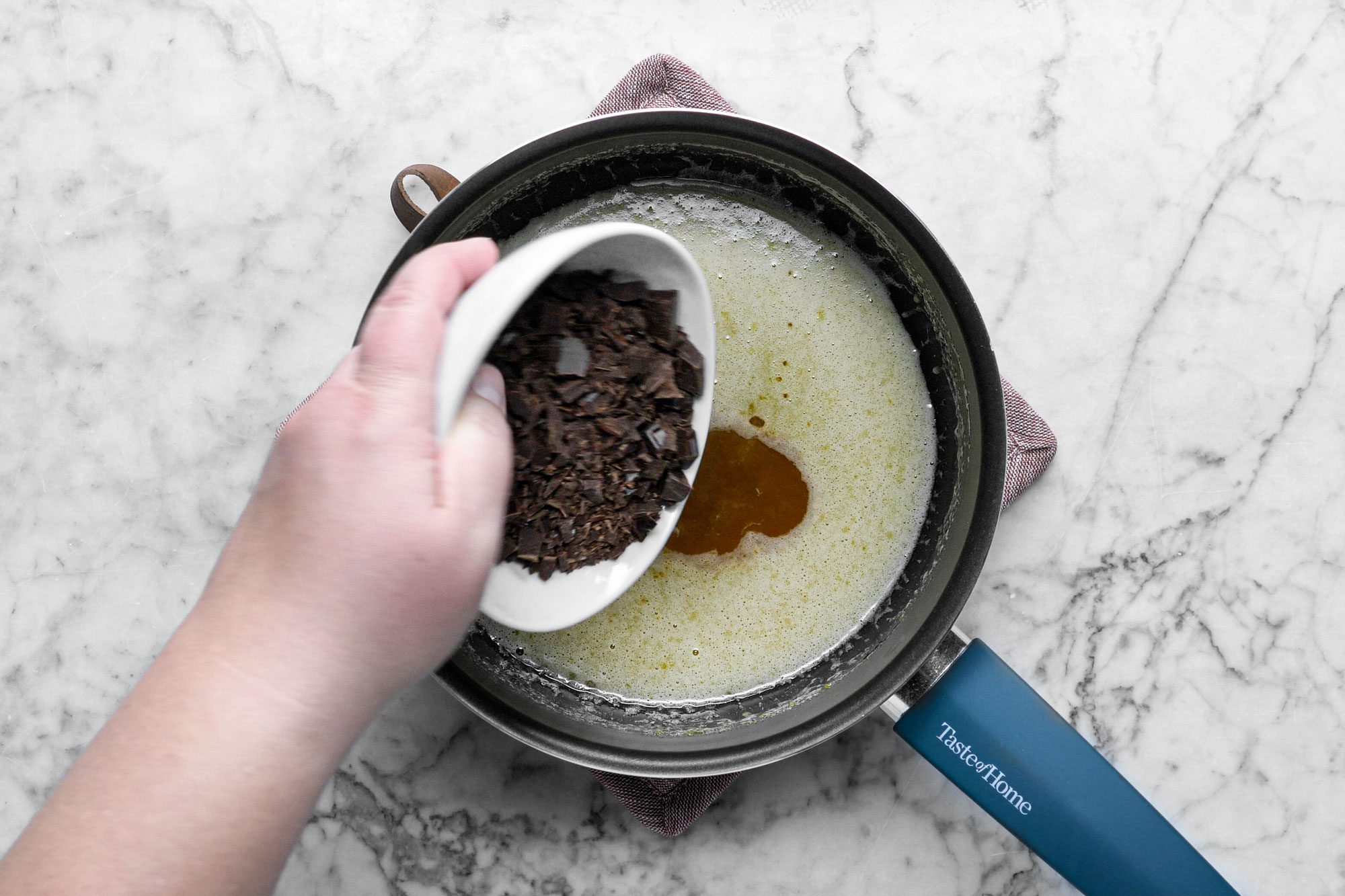 pouring chocolate into a saucepan filled with sugar syrup, marble background