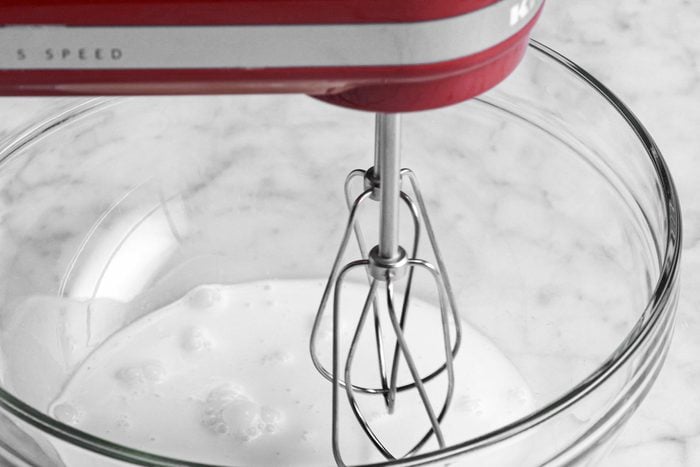 a hand mixer with large glass bowl filled with milk, marble background