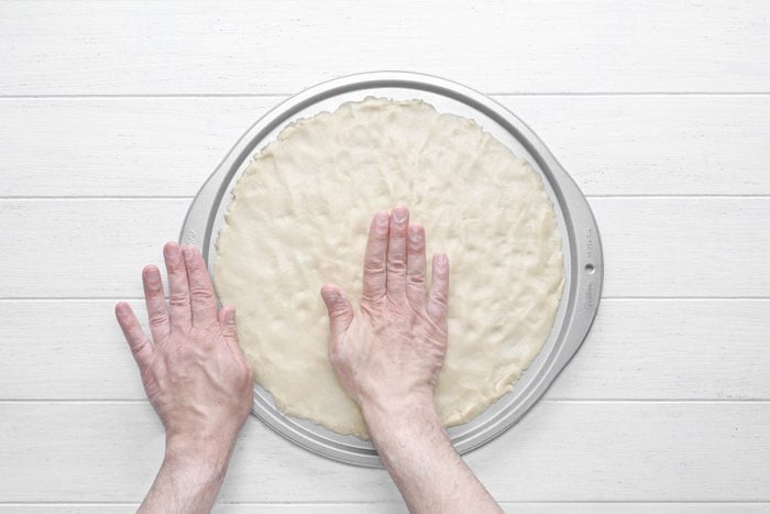 Patting the pizza dough on pan