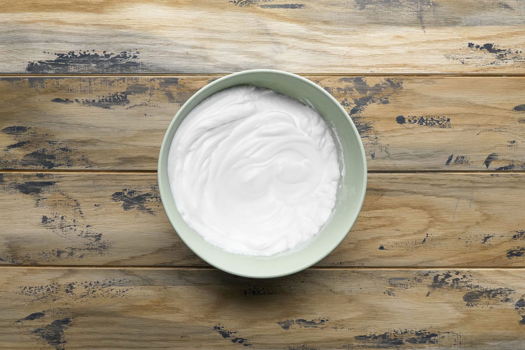 Egg whites stiff peak in a small bowl on a wooden table