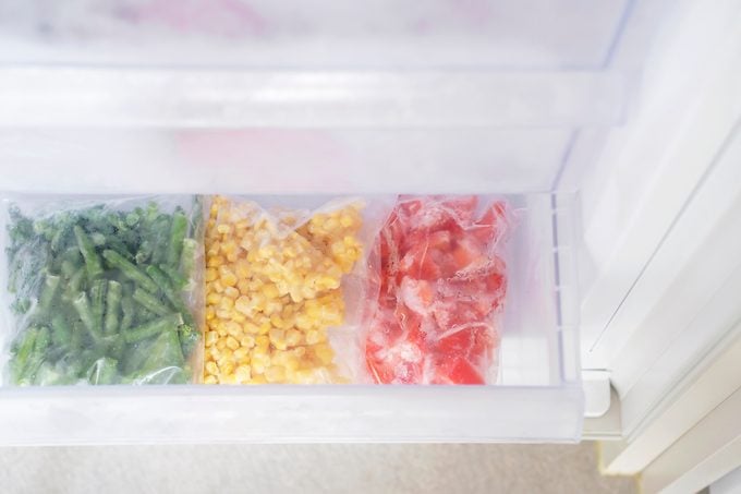 Frozen vegetables in plastic bags in freezer close-up, top view.