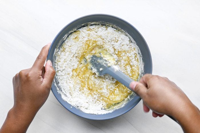 a person mixing egg mixture into flour in a large bowl using a spatula