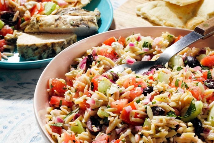 A spoon inside the bowl full of Greek-Orzo-Salad