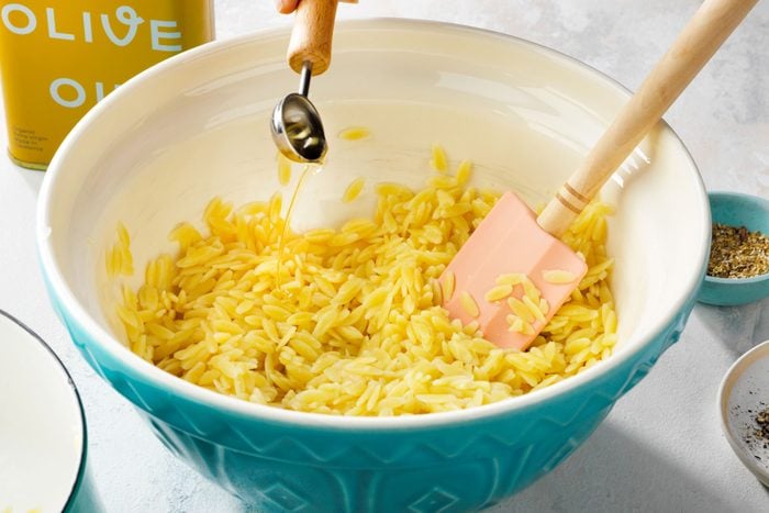 Adding olive oil in orzo, in a large bowl with a spatula