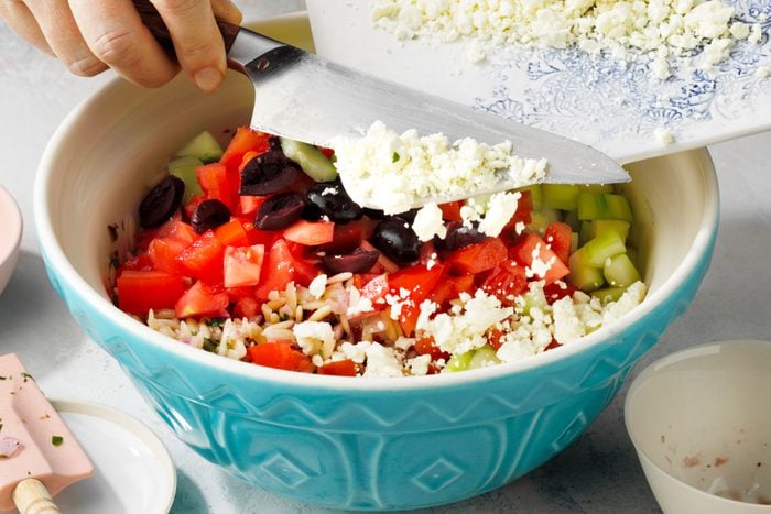 Adding cheese in the Orzo salad in a large bowl using a knife.