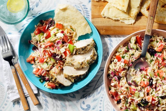 Greek Orzo Salad served on a table with bread and spoon on the side.