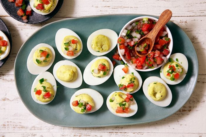 Guacamole Deviled Eggs in white plates places on a wooden tray
