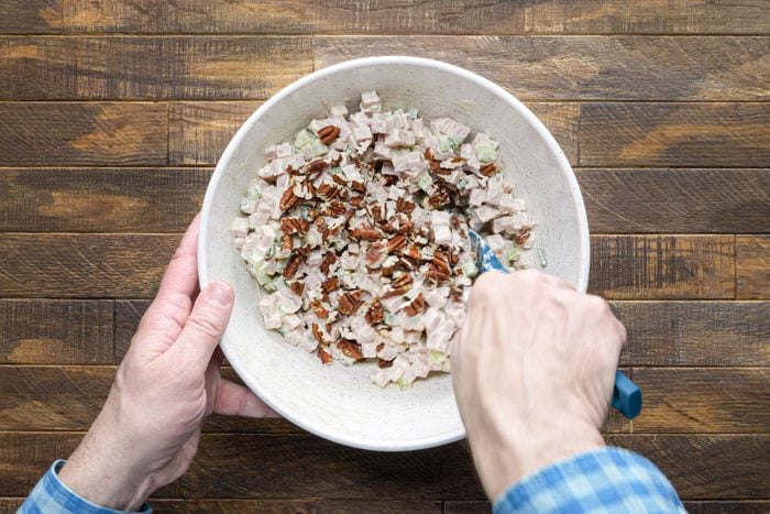 Mixing chopped pecans and almonds in diced ham using a spatula in a large bowl.