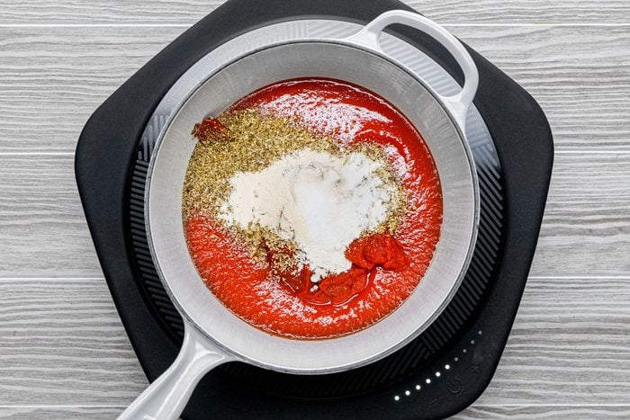 tomato sauce and paste, Italian seasoning, dried oregano, crushed fennel seed, onion powder, garlic powder and salt in a saucepan on an induction cooktop on wooden surface