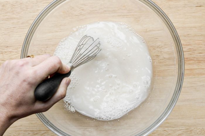mixing yeast, sugar and flour in warm water in a large glass bowl on a wooden surface