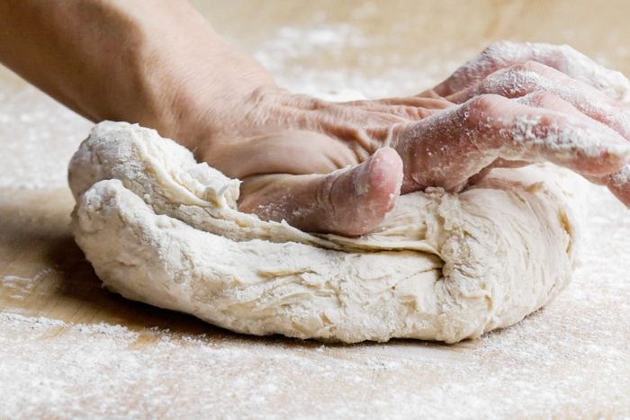 a person kneading the dough on a floured wooden surface